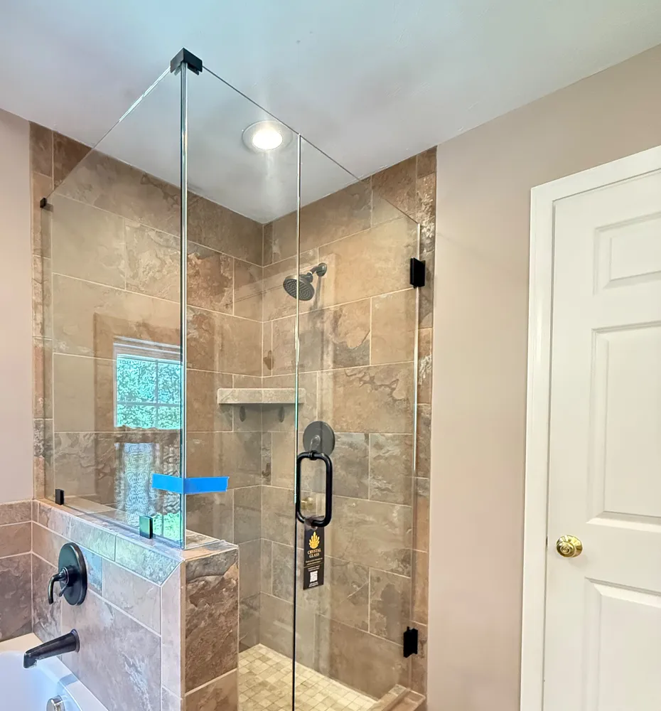 The same travertine tiled shower after, with a custom glass panel and door installed