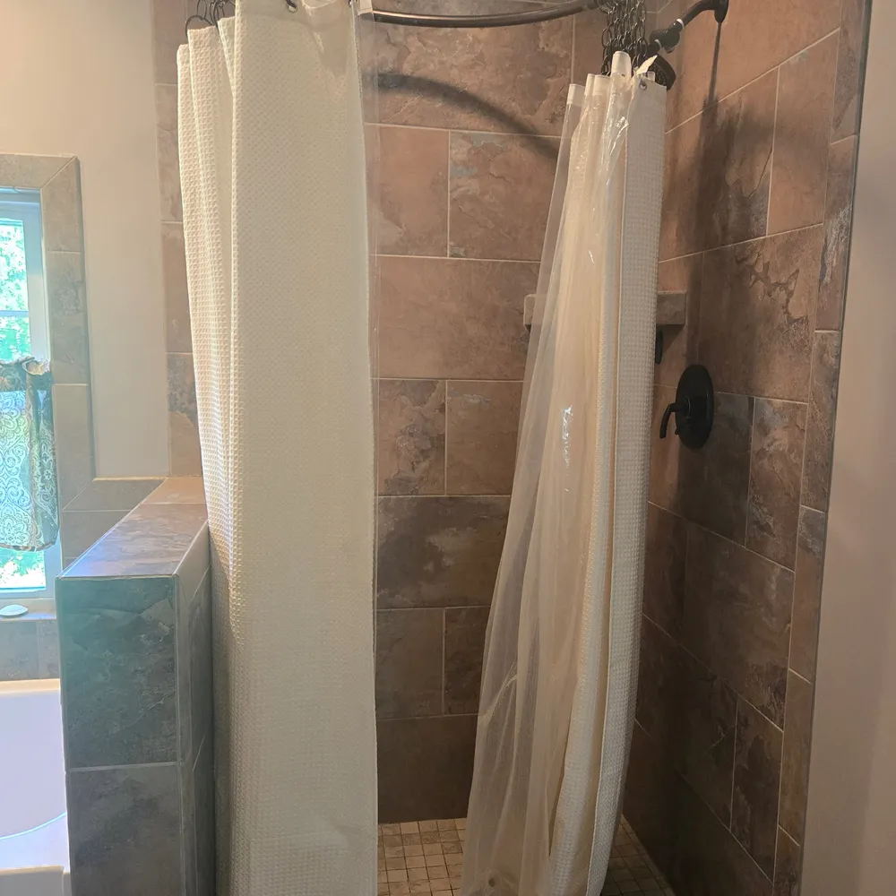 Tub shower closed off by a fabric curtain on a circular rod, before the glass