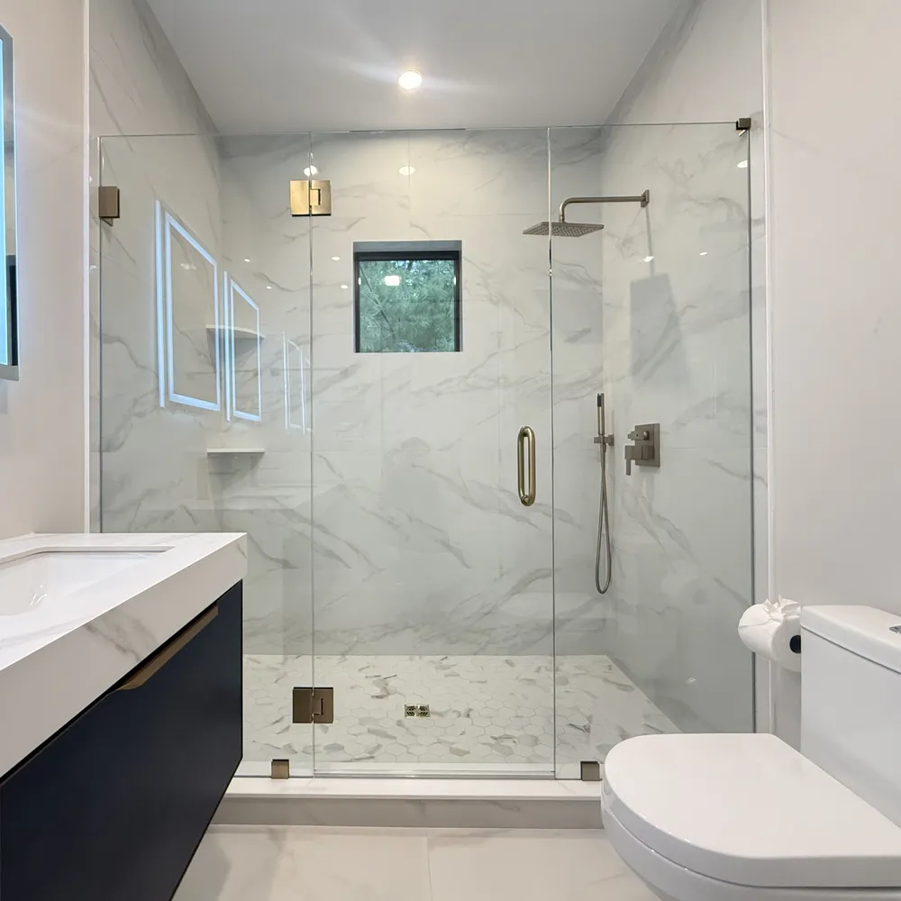 The same marble shower after, closed with a frameless corner enclosure and brushed gold hardware