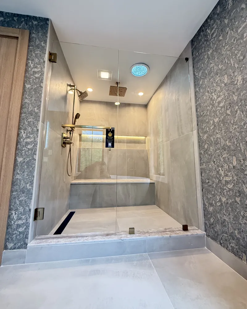 Walk in frameless glass panel on a grey stone shower with a built in bench