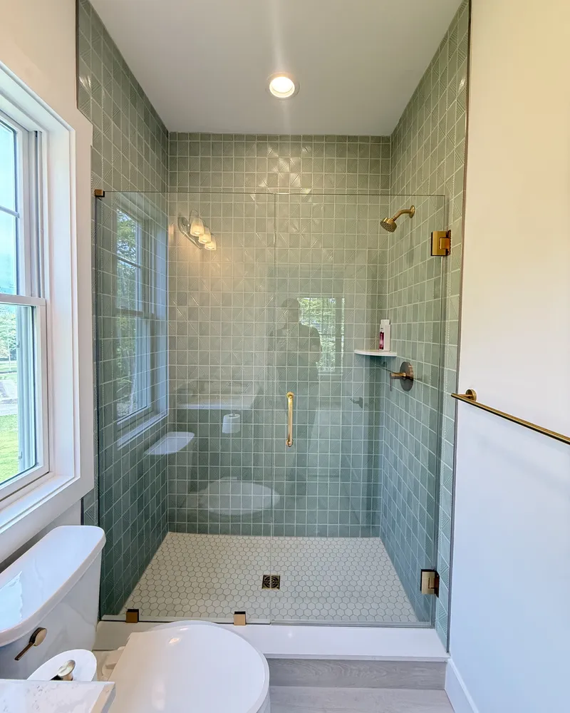 Frameless glass door on a green tiled shower with brushed gold fixtures