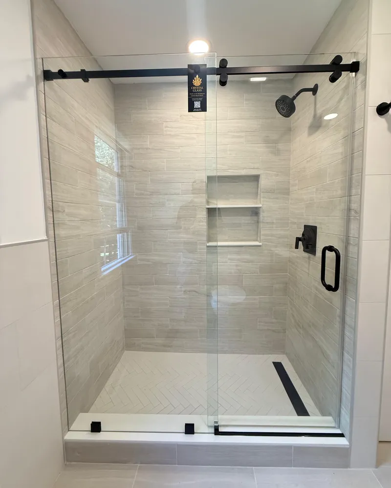 Sliding glass shower door on a black track over a tiled alcove shower