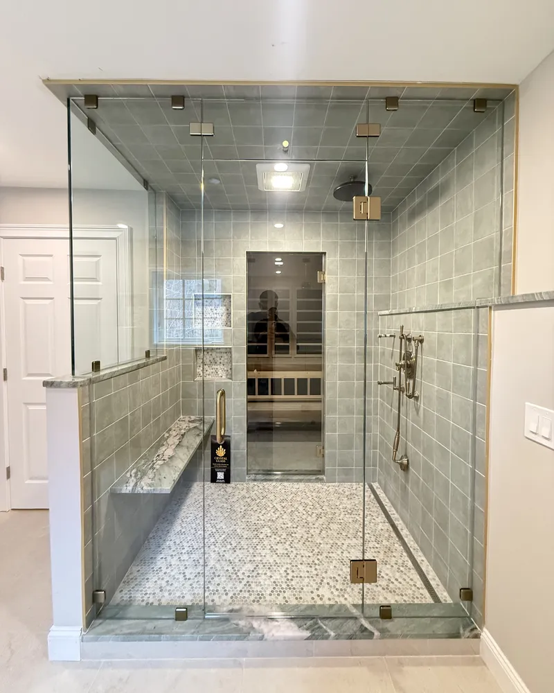 Full height frameless enclosure on a tiled shower with gold clamps and a stone bench